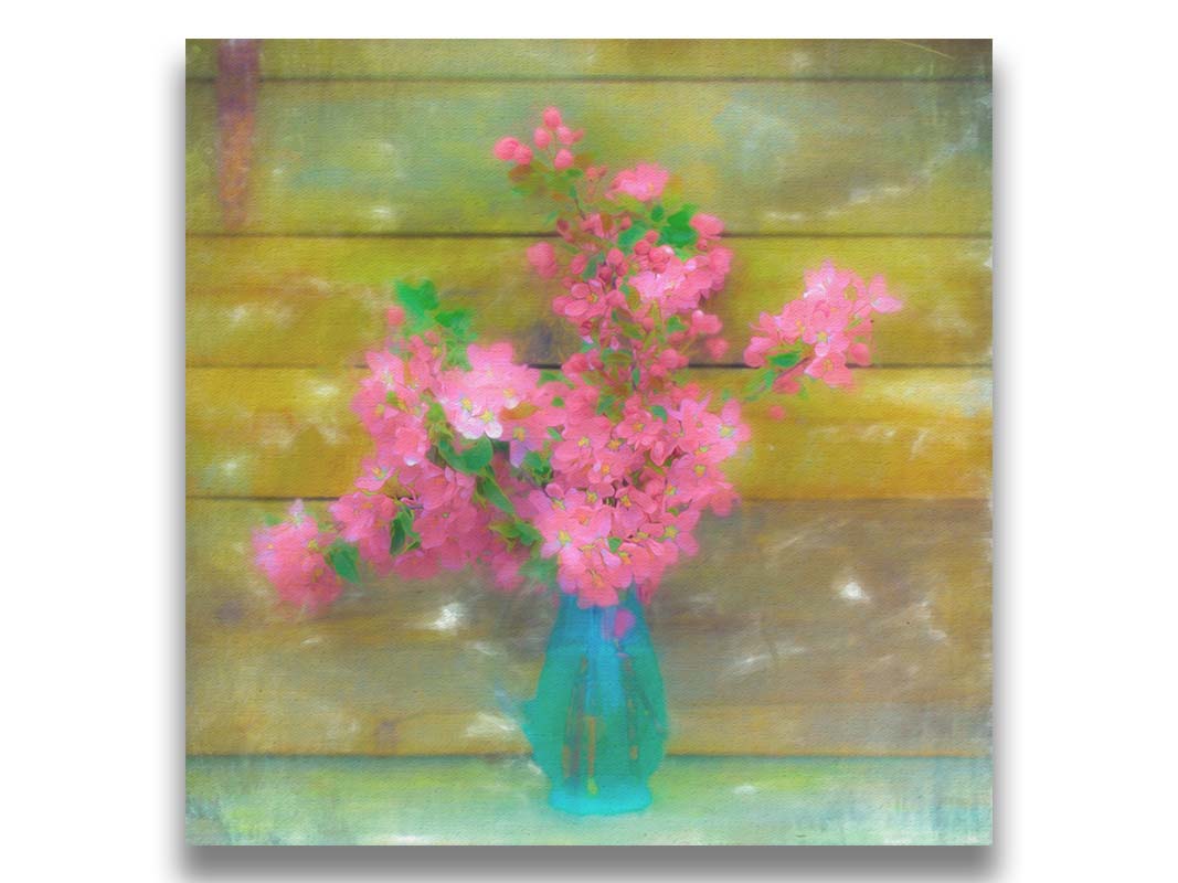 A photograph of a blue vase of bright pink flower blossoms against a yellow painted wooden wall. Printed on canvas.