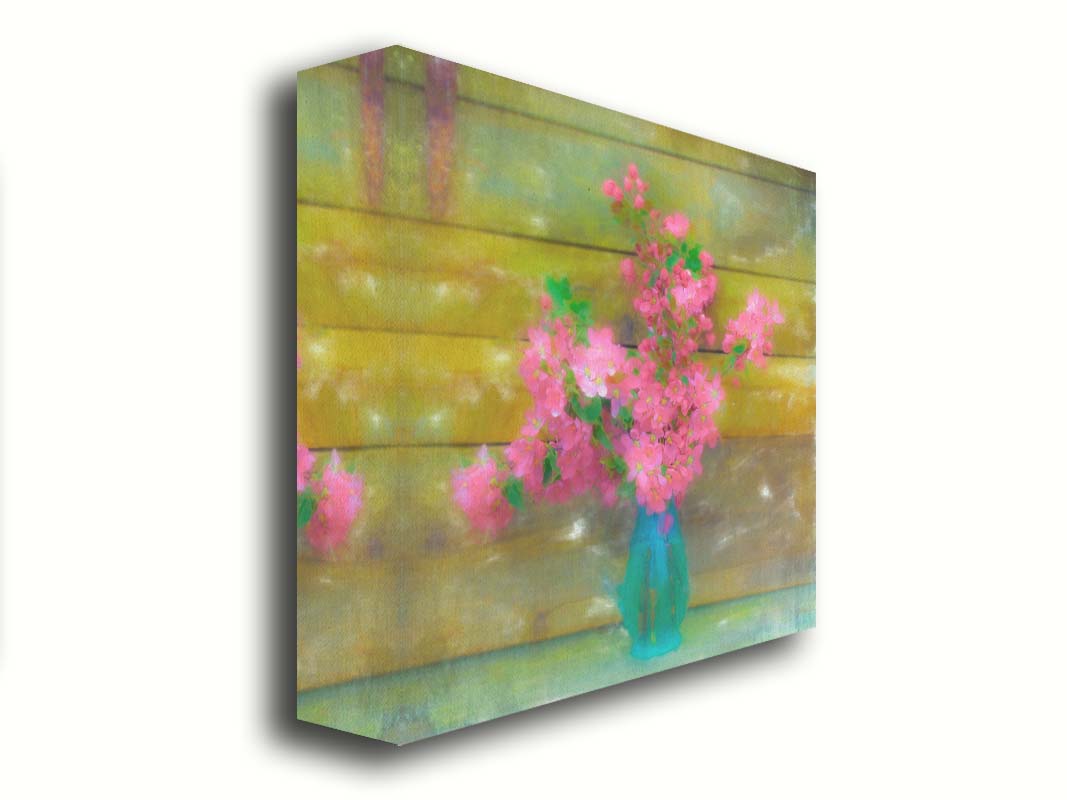 A photograph of a blue vase of bright pink flower blossoms against a yellow painted wooden wall. Printed on canvas.