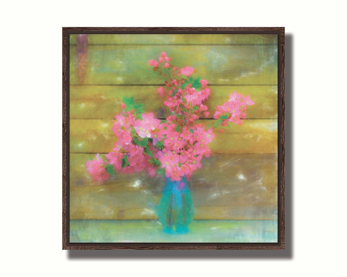 A photograph of a blue vase of bright pink flower blossoms against a yellow painted wooden wall. Printed on canvas in a float frame.