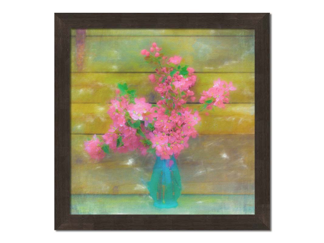 A photograph of a blue vase of bright pink flower blossoms against a yellow painted wooden wall. Printed on canvas and framed.