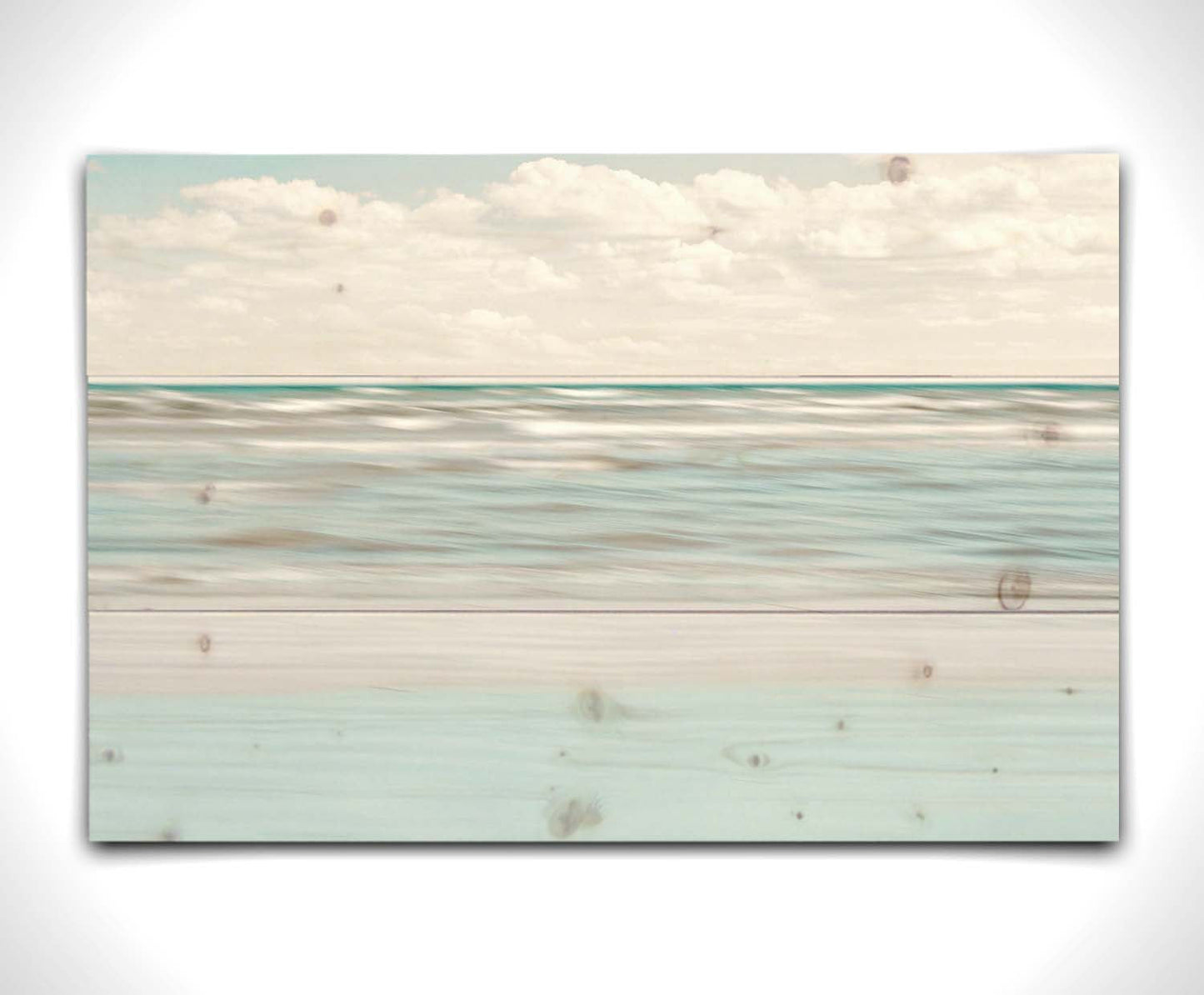 A photo of the ocean, and the line formed at the horizon where its color cuts across the sky of fluffy, white clouds. Printed on a wood pallet.