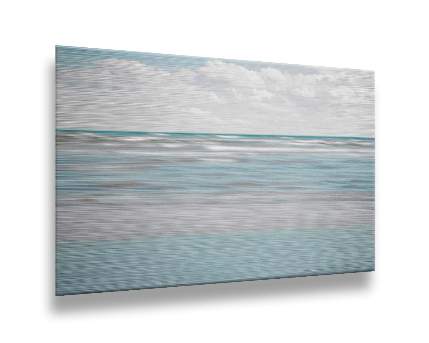 A photo of the ocean, and the line formed at the horizon where its color cuts across the sky of fluffy, white clouds. Printed on metal.