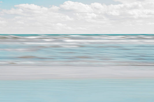 A photo of the ocean, and the line formed at the horizon where its color cuts across the sky of fluffy, white clouds.