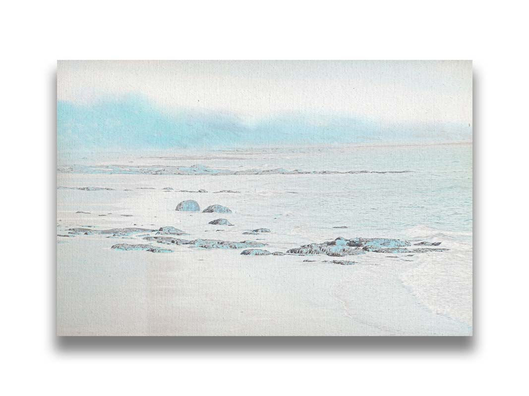 A photo of a rocky beach with a pale blue palette. The sea is calm and washing over the sand and rocks. Printed on canvas.