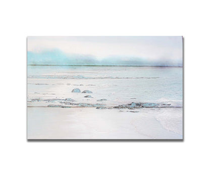 A photo of a rocky beach with a pale blue palette. The sea is calm and washing over the sand and rocks. Printed on a box board.