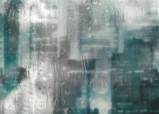 A photo looking across a city from a window, edited to have a blurry, inky quality and overlaid with rainy wet glass. 