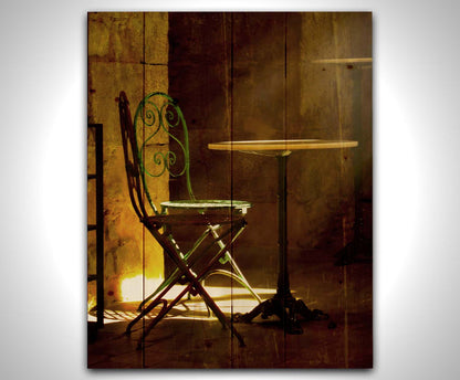 A photo of chairs around a small table, illuminated by light pouring in through the window. Printed on a wood pallet.