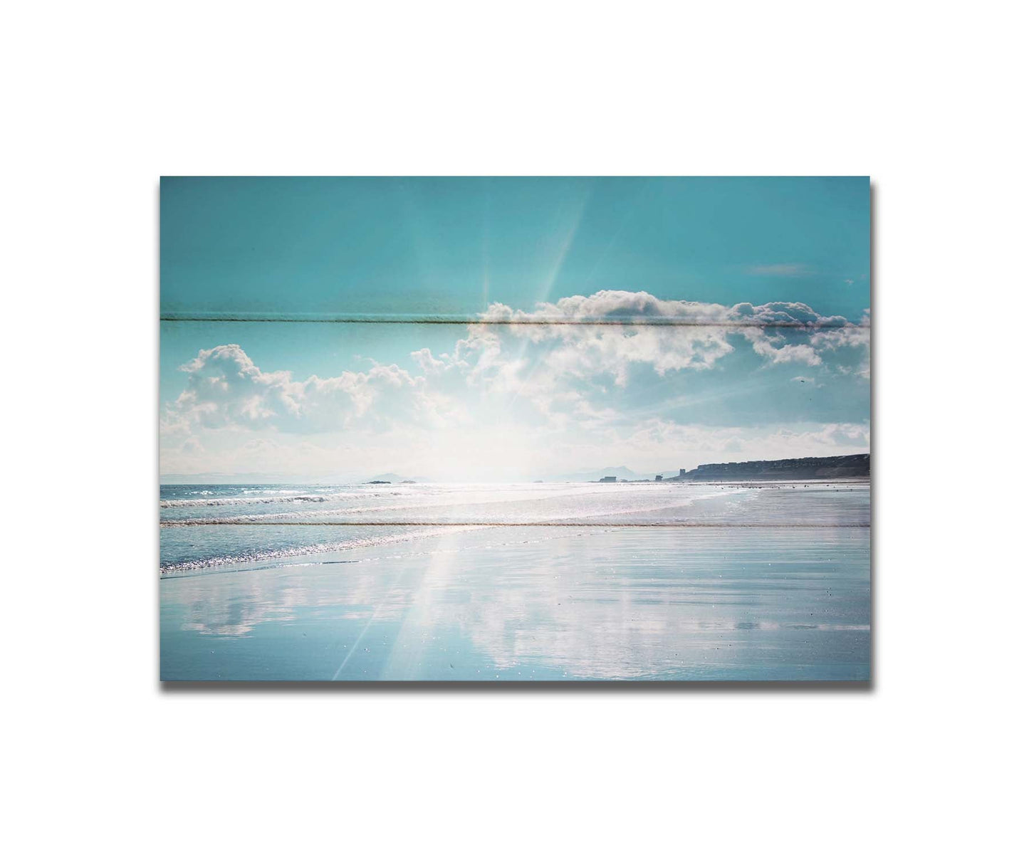 A photo of an ocean view, with a town on the coast. The sun is getting low in the sky, just before sunset, and the light is reflecting off the blue water and wet sand. Printed on a box board.