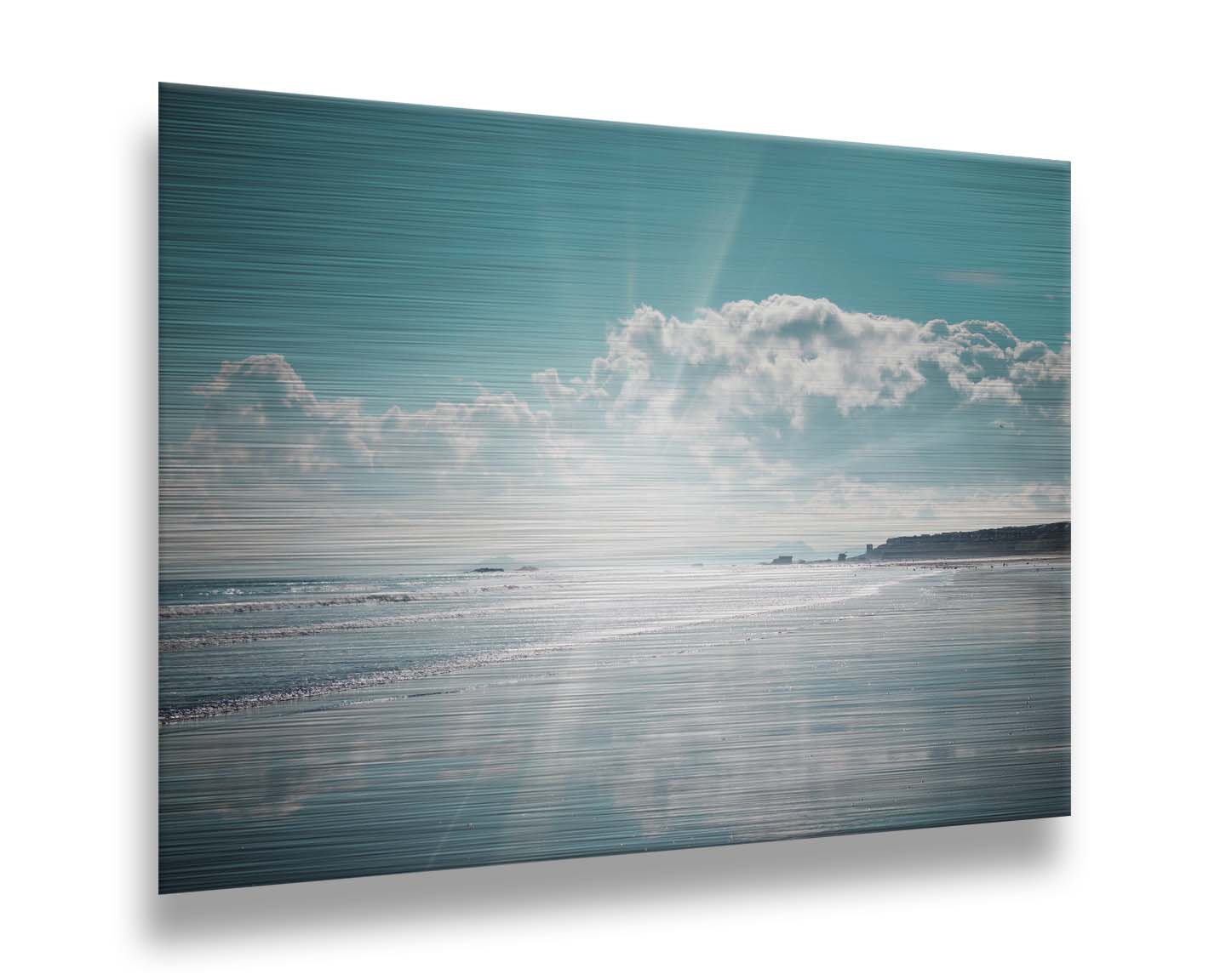 A photo of an ocean view, with a town on the coast. The sun is getting low in the sky, just before sunset, and the light is reflecting off the blue water and wet sand. Printed on metal.