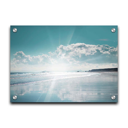 A photo of an ocean view, with a town on the coast. The sun is getting low in the sky, just before sunset, and the light is reflecting off the blue water and wet sand. Printed on acrylic.