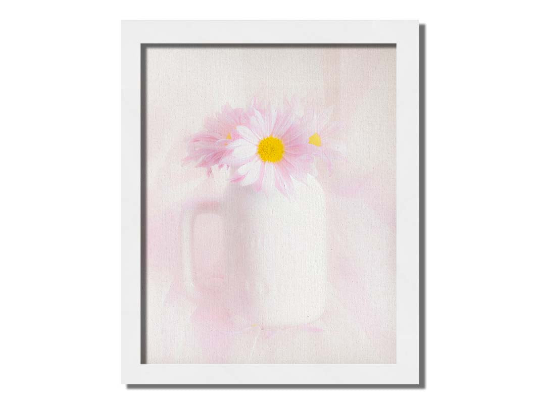 A photo of a white vase with pink daisies in a soft pink background. Printed on canvas and framed.