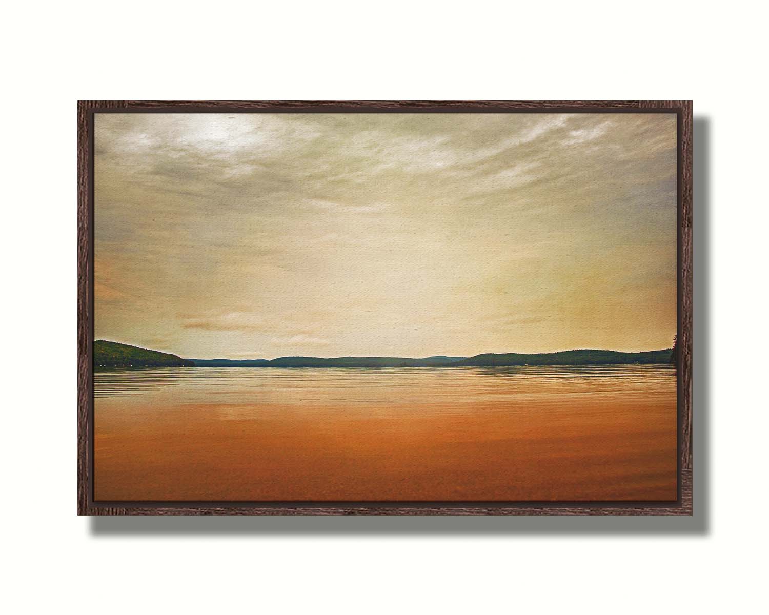 A photograph looking out at the sea and sky. The sky is cloudy and a warm gray, while the sea reflects a brilliant orange. Coastlines of trees can be seen in the distance. Printed on canvas in a float frame.