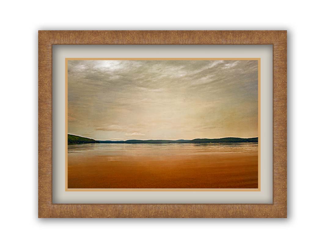 A photograph looking out at the sea and sky. The sky is cloudy and a warm gray, while the sea reflects a brilliant orange. Coastlines of trees can be seen in the distance. Printed on paper, matted, and framed.