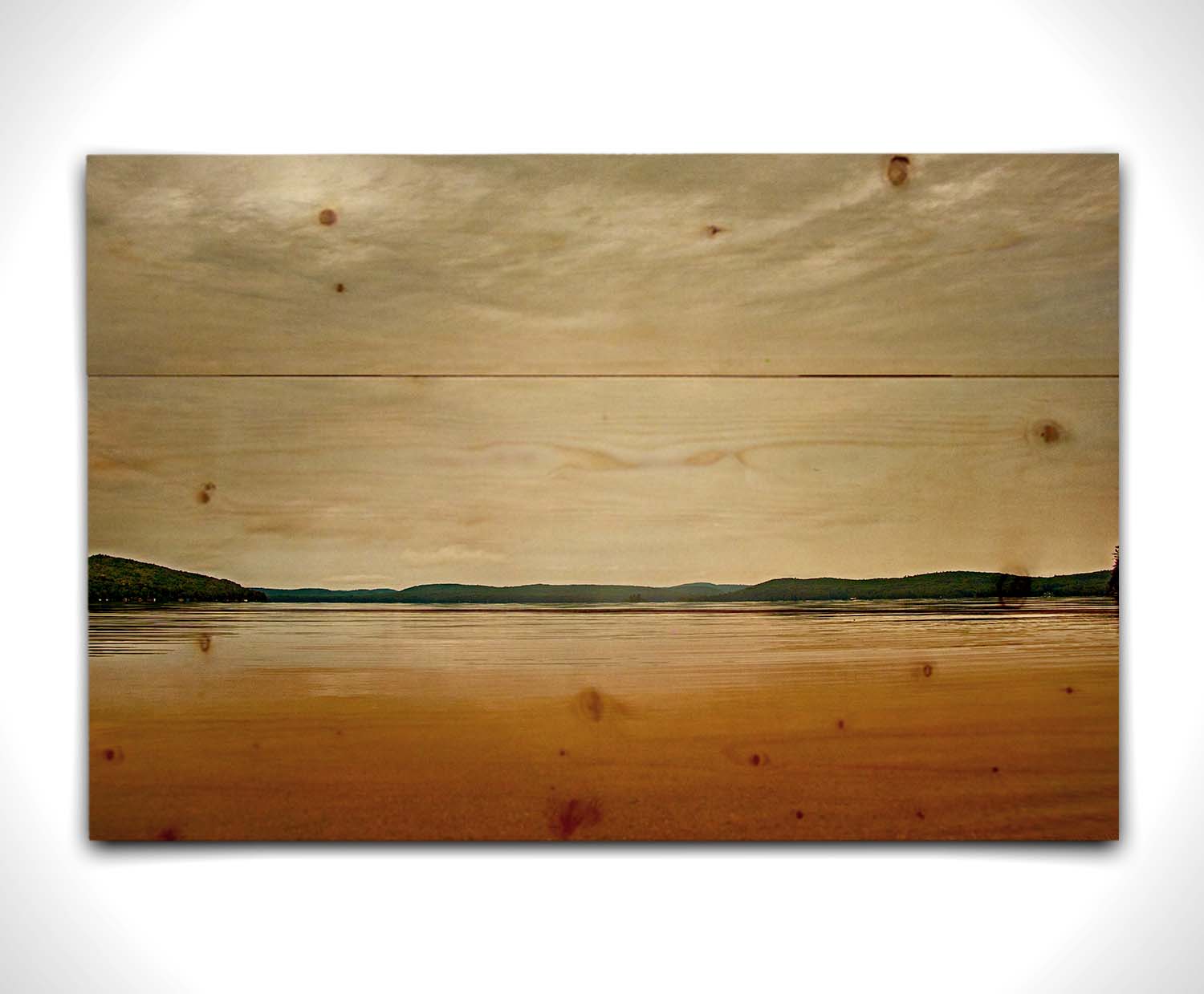 A photograph looking out at the sea and sky. The sky is cloudy and a warm gray, while the sea reflects a brilliant orange. Coastlines of trees can be seen in the distance. Printed on a wood pallet.