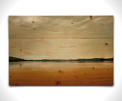 A photograph looking out at the sea and sky. The sky is cloudy and a warm gray, while the sea reflects a brilliant orange. Coastlines of trees can be seen in the distance. Printed on a wood pallet.