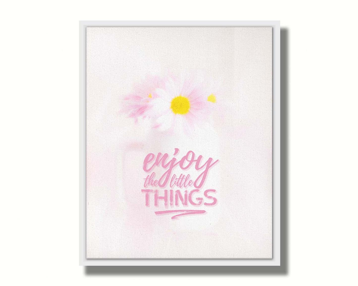 A photo of a white vase with pink daisies in a soft pink background, superimposed with the phrase "enjoy the little things". Printed on canvas in a float frame.