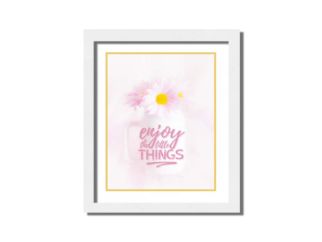 A photo of a white vase with pink daisies in a soft pink background, superimposed with the phrase "enjoy the little things". Printed on paper, matted, and framed.