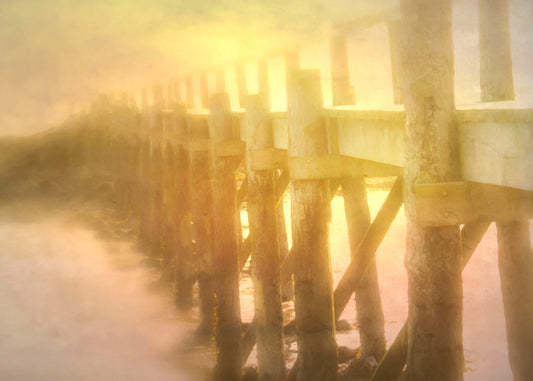 A photo of a pier trailing off into the water, lit by the sunset. 