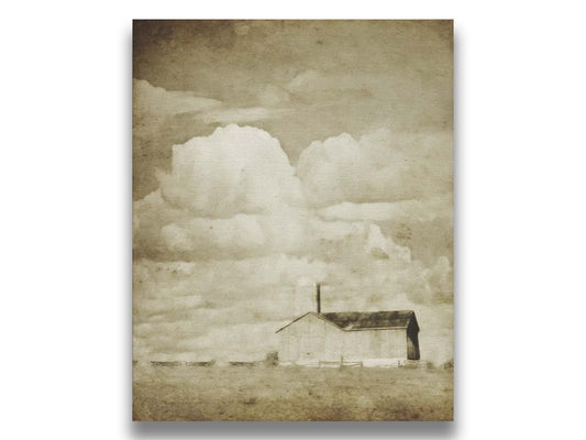 A sepia photo of a barn under a wide, open sky with large, fluffy clouds. Printed on canvas.