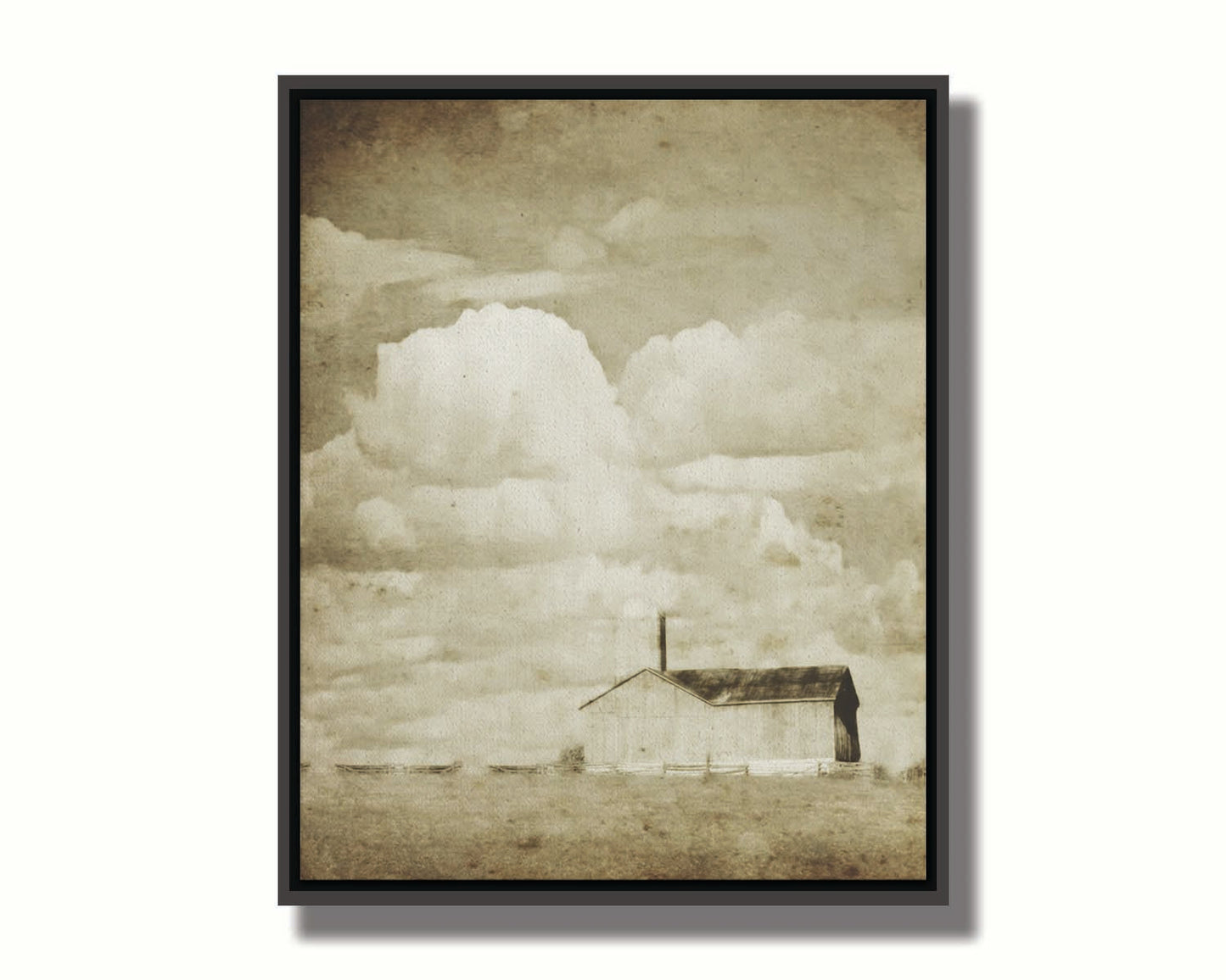 A sepia photo of a barn under a wide, open sky with large, fluffy clouds. Printed on canvas in a float frame.