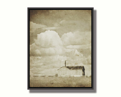 A sepia photo of a barn under a wide, open sky with large, fluffy clouds. Printed on canvas in a float frame.