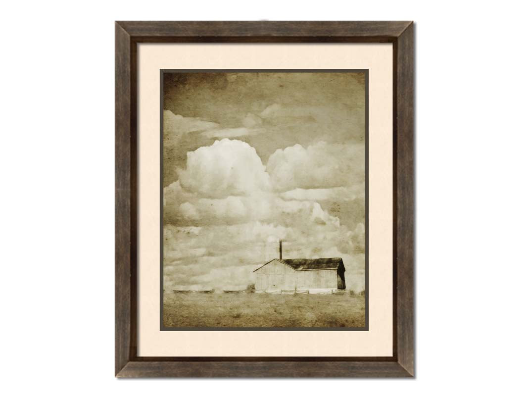 A sepia photo of a barn under a wide, open sky with large, fluffy clouds. Printed on paper, matted, and framed.