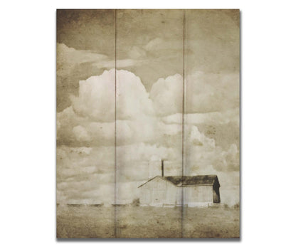 A sepia photo of a barn under a wide, open sky with large, fluffy clouds. Printed on a box board.