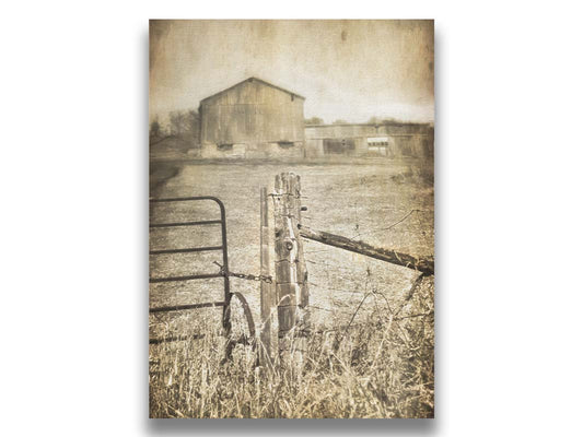 A photo of a farm fence and gate, with a large barn in the background in sepia tone. Printed on canvas.