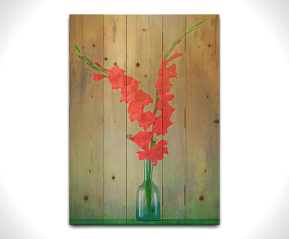 A photo of two red gladiolus flower spikes in a small blue vase. Printed on a wood pallet.