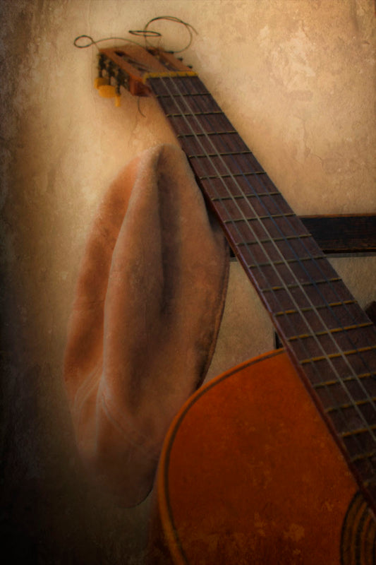 A photo of an acoustic guitar and a hat, sitting on a chair.