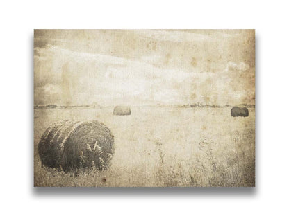 A sepia photo of a wide, open field with several hay bales. Printed on canvas.