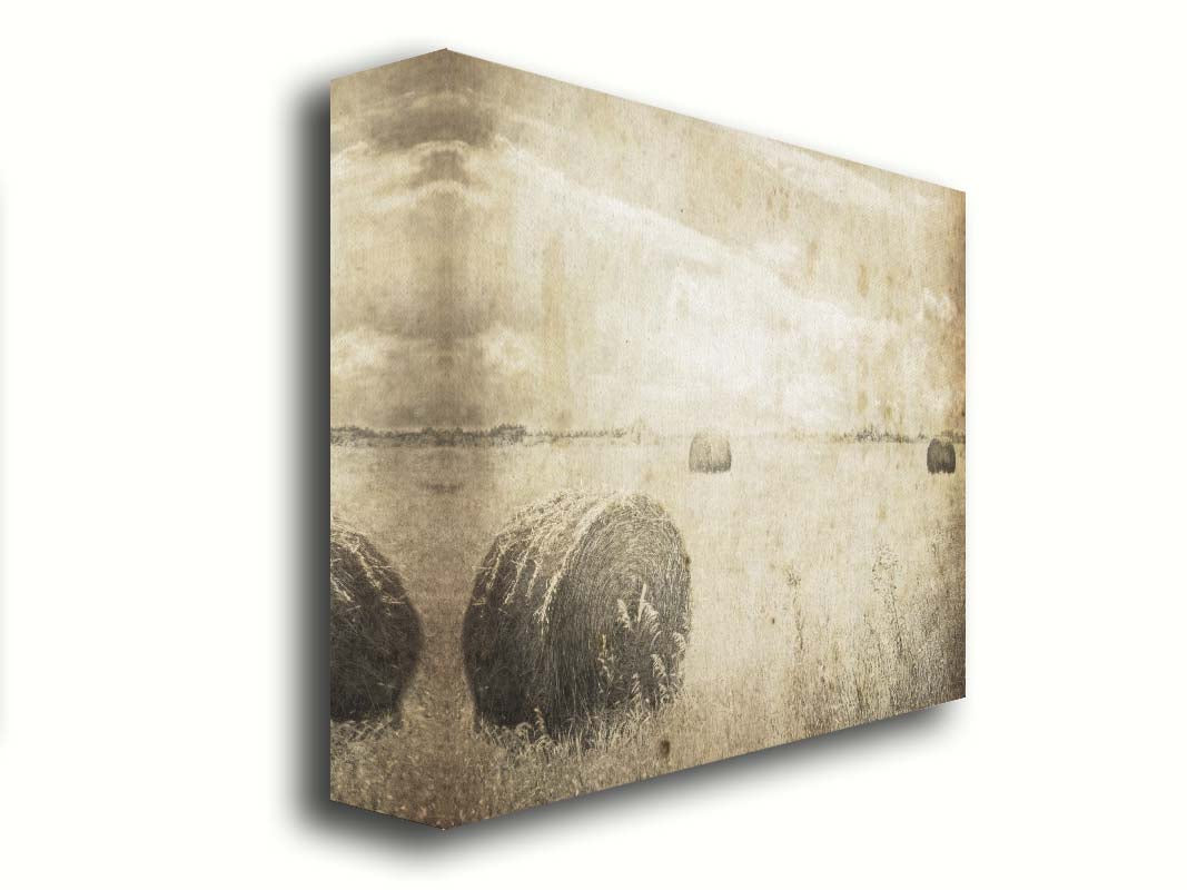 A sepia photo of a wide, open field with several hay bales. Printed on canvas.