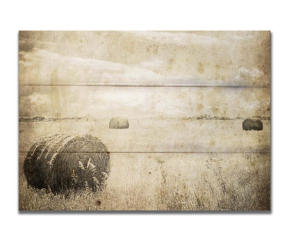 A sepia photo of a wide, open field with several hay bales. Printed on a box board.