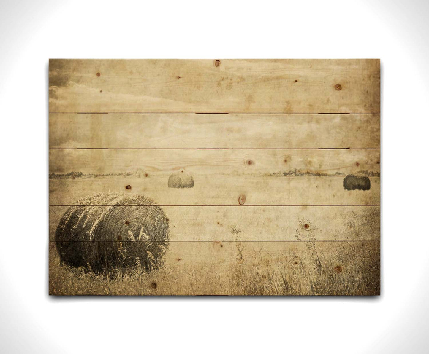 A sepia photo of a wide, open field with several hay bales. Printed on a wood pallet.