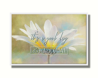 A photo of a white daisy in the sunlight, against a soft green background. It is overlaid with the phrase "It's a good day, let's make it great!" Printed on canvas in a float frame.