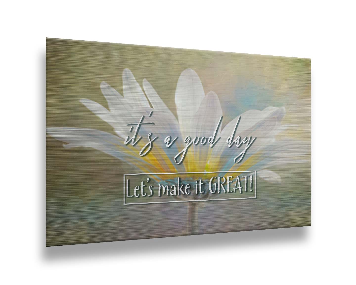 A photo of a white daisy in the sunlight, against a soft green background. It is overlaid with the phrase "It's a good day, let's make it great!" Printed on metal.