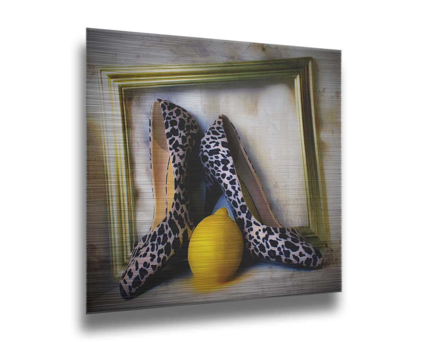 A still life photo of a pair of shoe heels in front of a gold picture frame, accompanied by a lemon. Printed on metal.