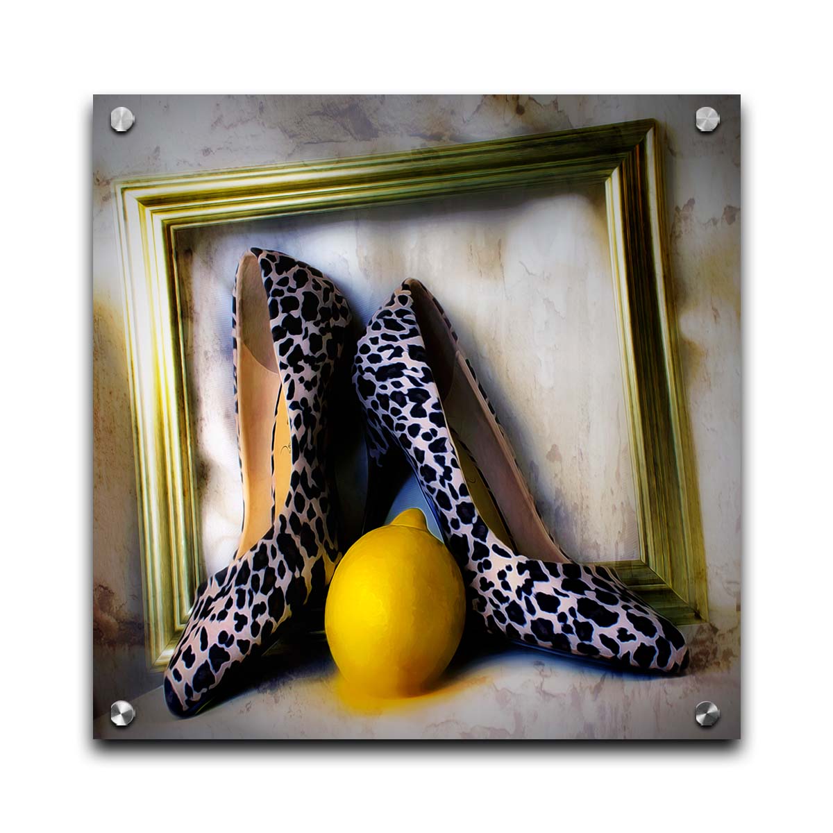 A still life photo of a pair of shoe heels in front of a gold picture frame, accompanied by a lemon. Printed on acrylic.