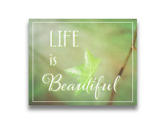 A photograph of a green leaf in soft lighting. The photo is overlaid with white text reading "life is beautiful". Printed on canvas.