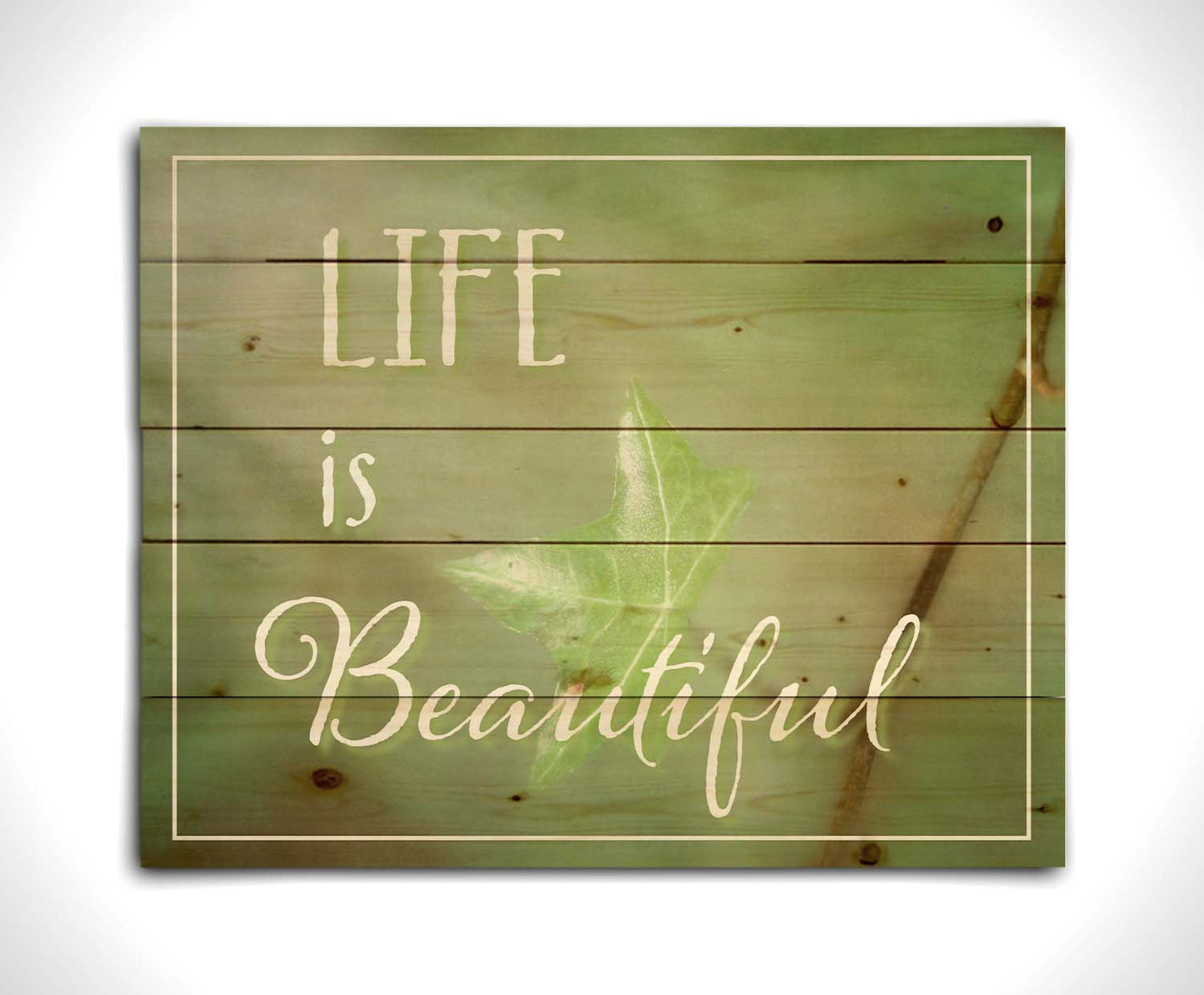 A photograph of a green leaf in soft lighting. The photo is overlaid with white text reading "life is beautiful". Printed on a wood pallet.