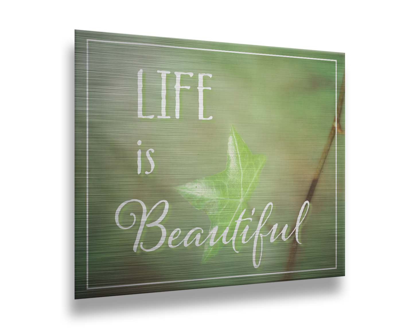 A photograph of a green leaf in soft lighting. The photo is overlaid with white text reading "life is beautiful". Printed on metal.