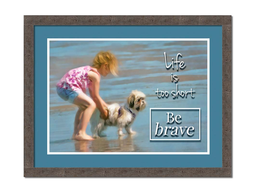 A photograph of a small child and a dog at the beach overlaid with the phrase "life is too short, be brave". Printed on paper, matted, and framed.