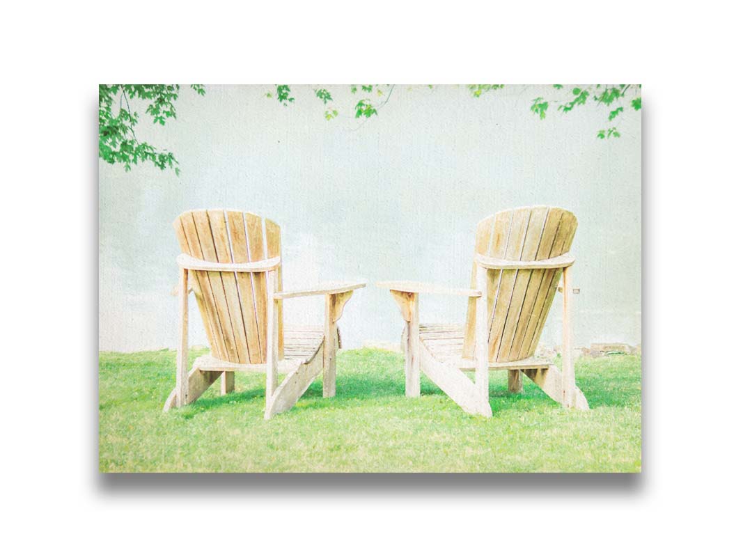 A photo of two wood lawn chairs, sitting on bright green grass, facing a lake. Printed on canvas.