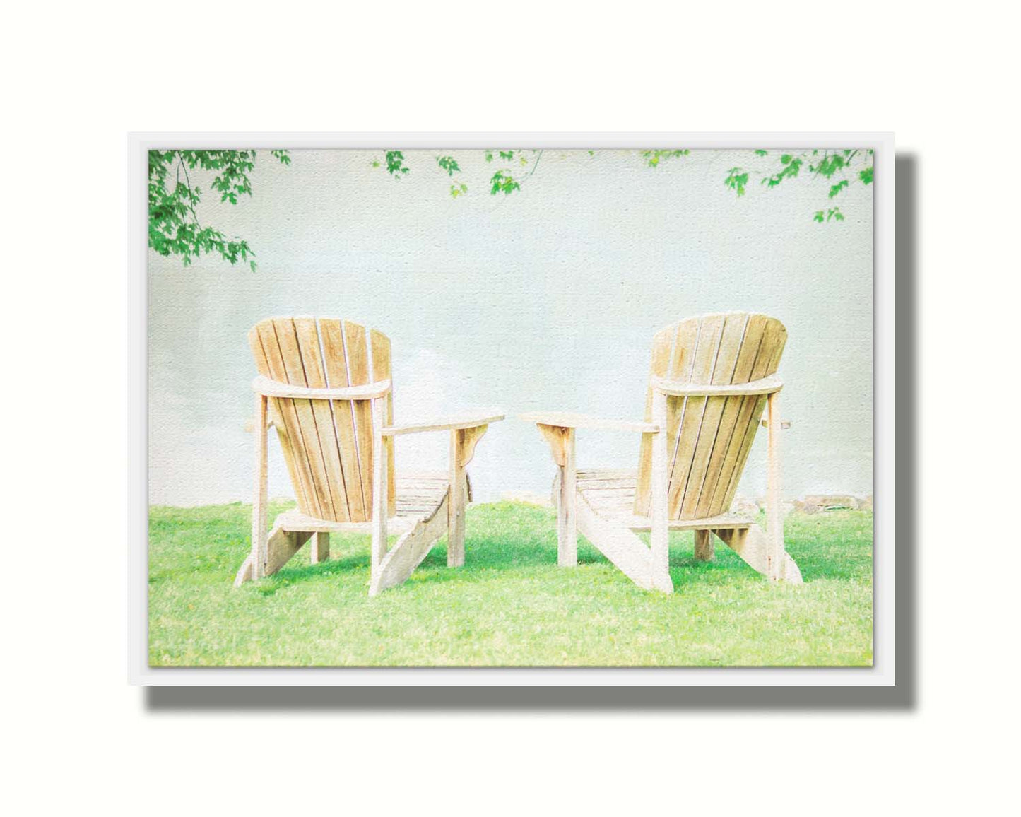 A photo of two wood lawn chairs, sitting on bright green grass, facing a lake. Printed on canvas in a float frame.