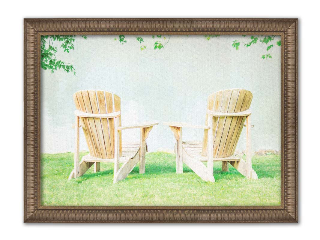 A photo of two wood lawn chairs, sitting on bright green grass, facing a lake. Printed on canvas and framed.