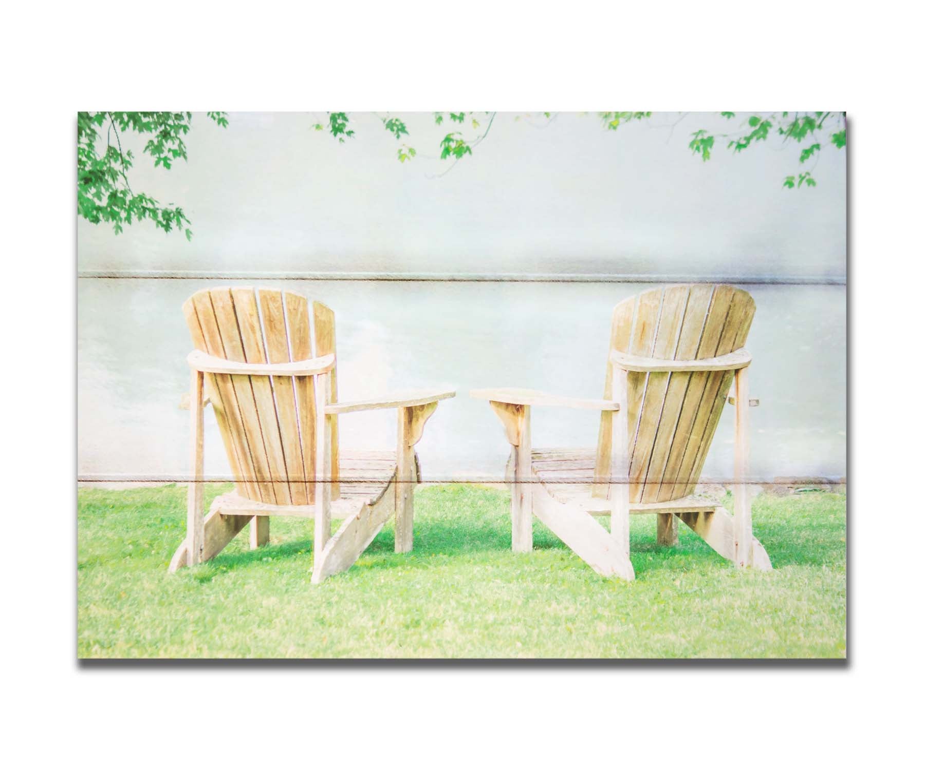 A photo of two wood lawn chairs, sitting on bright green grass, facing a lake. Printed on a box board.