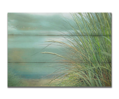 A photo of a tall grass plant on the beach, with the sea and cloudy skies in the background as seagulls fly above. Printed on a box board.