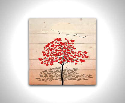 A graphic art piece of a tree with red hearts for leaves against a pink and white background, as birds fly overhead. Printed on a wood pallet.