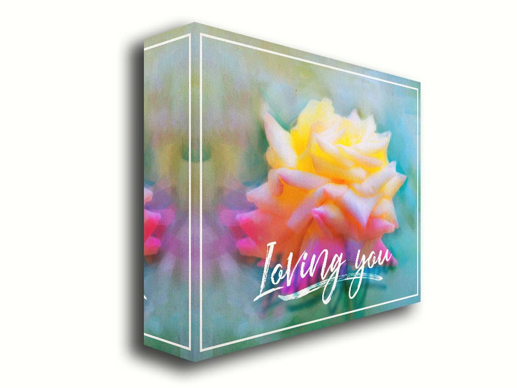 A photo of a pink and yellow rose against a blue background, edited to have a painterly appearance. It is overlaid with a white border and text reading "Loving you." Printed on canvas.