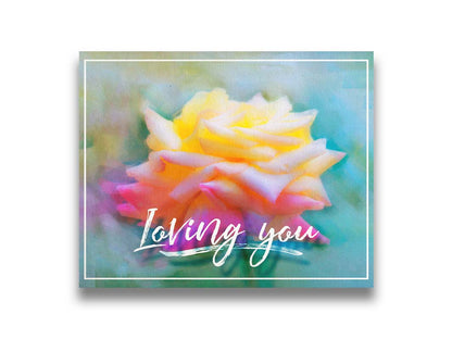 A photo of a pink and yellow rose against a blue background, edited to have a painterly appearance. It is overlaid with a white border and text reading "Loving you." Printed on canvas.